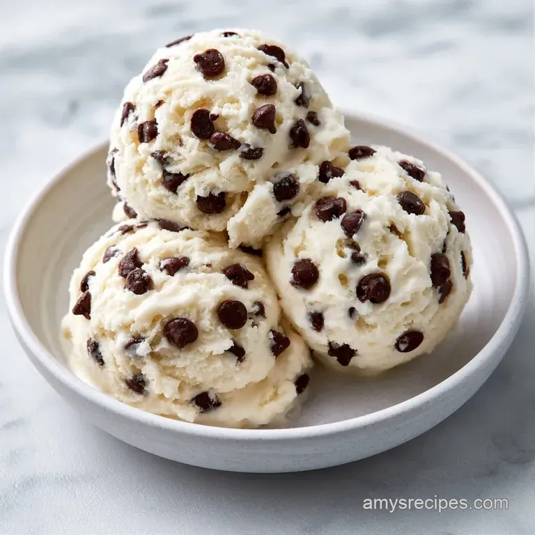 Three neat scoops of pale vanilla ice cream in a crystal bowl, garnished with a bright red cherry and mint leaf.